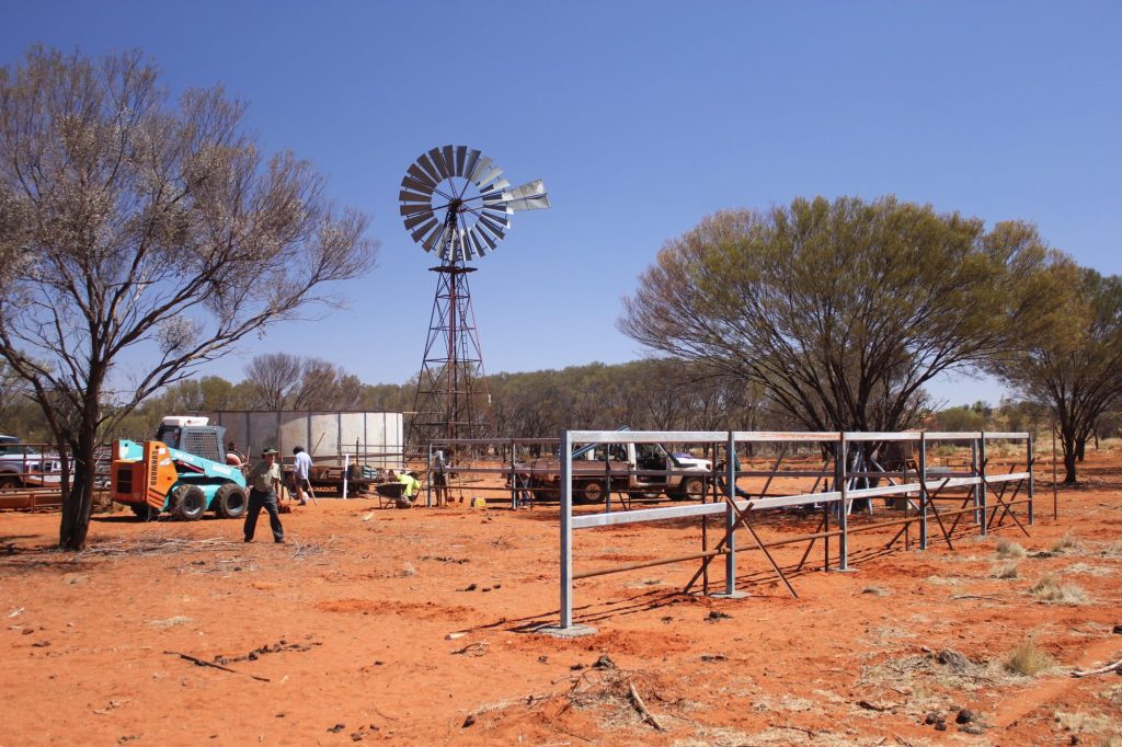 A windmill, water tank and cattle yards at a station bore on red earth