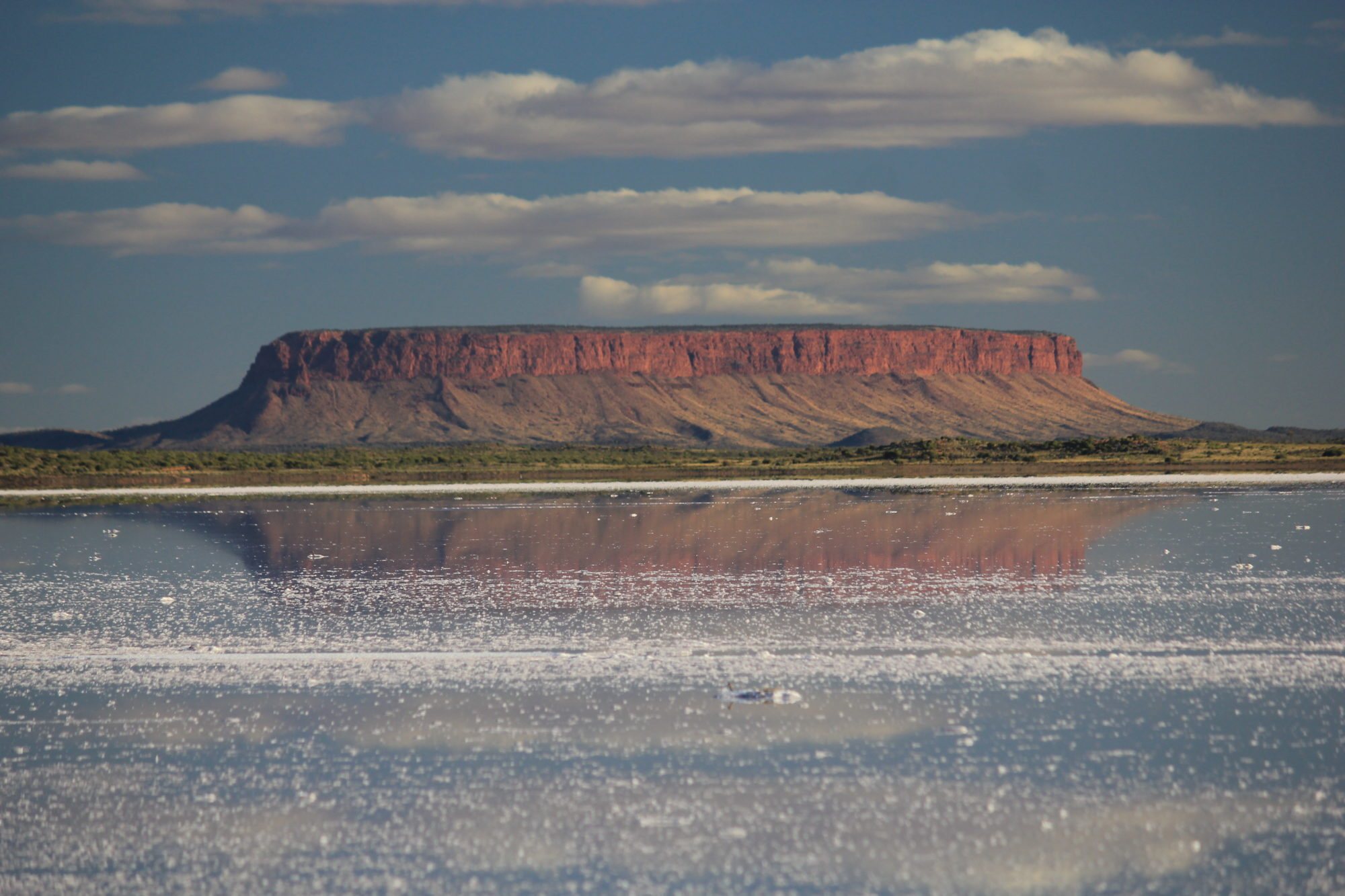 Mount Conner reflected in the still water of a salt lake under scattered cloud