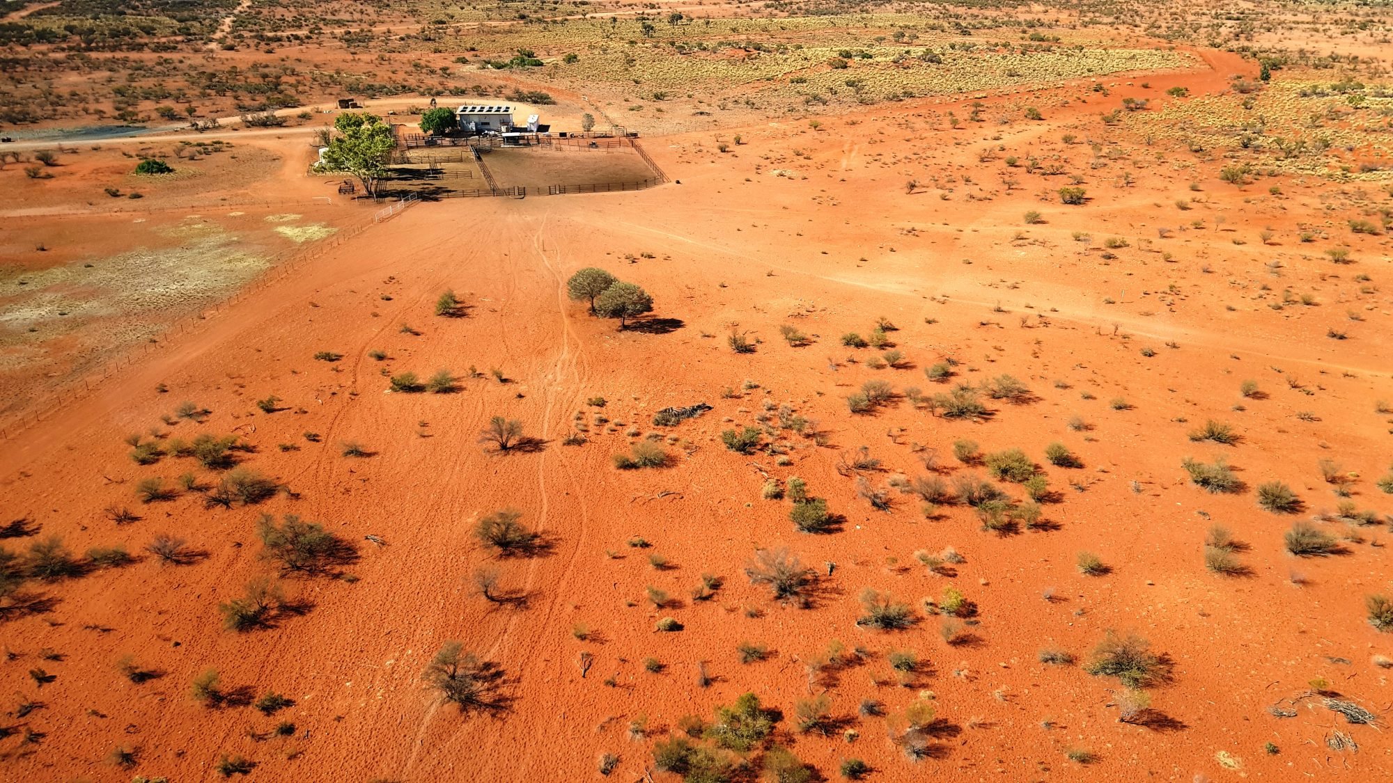 Aerial view across red sand country towards a station outstation