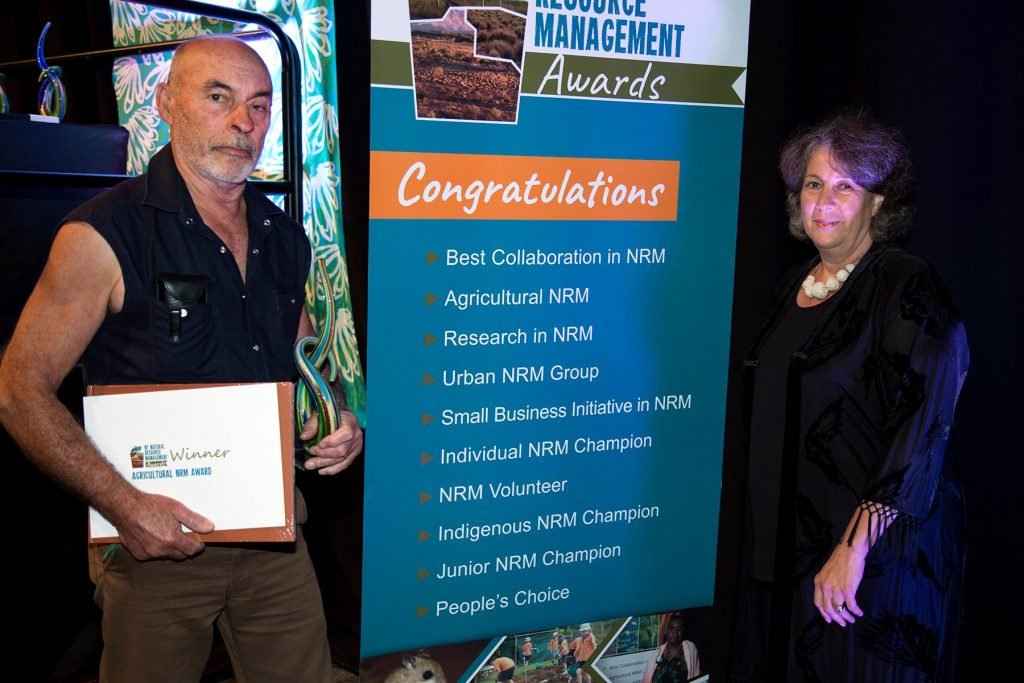 Two award recipients beside the Natural Resource Management awards banner, holding a trophy and certificate.