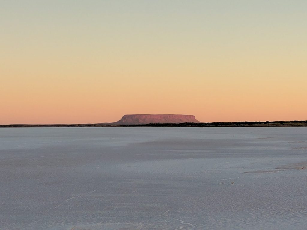 Mount Conner on the horizon across a still salt lake under a peach dusk sky