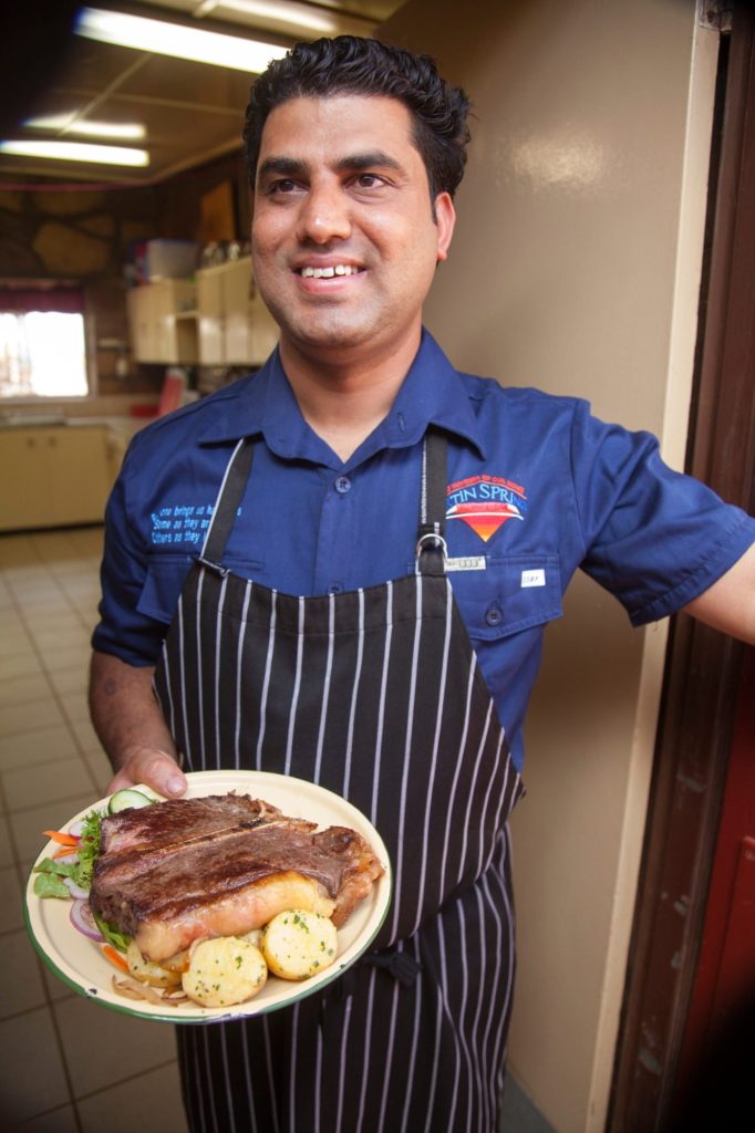 A cook in the Curtin Springs kitchen holding a plate of steak and vegetables.
