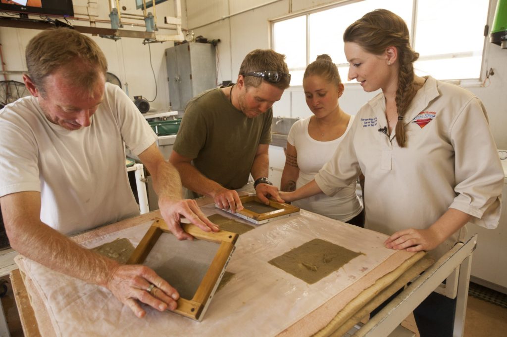 Visitors on a paper tour pressing a mould onto a felt beside their guide
