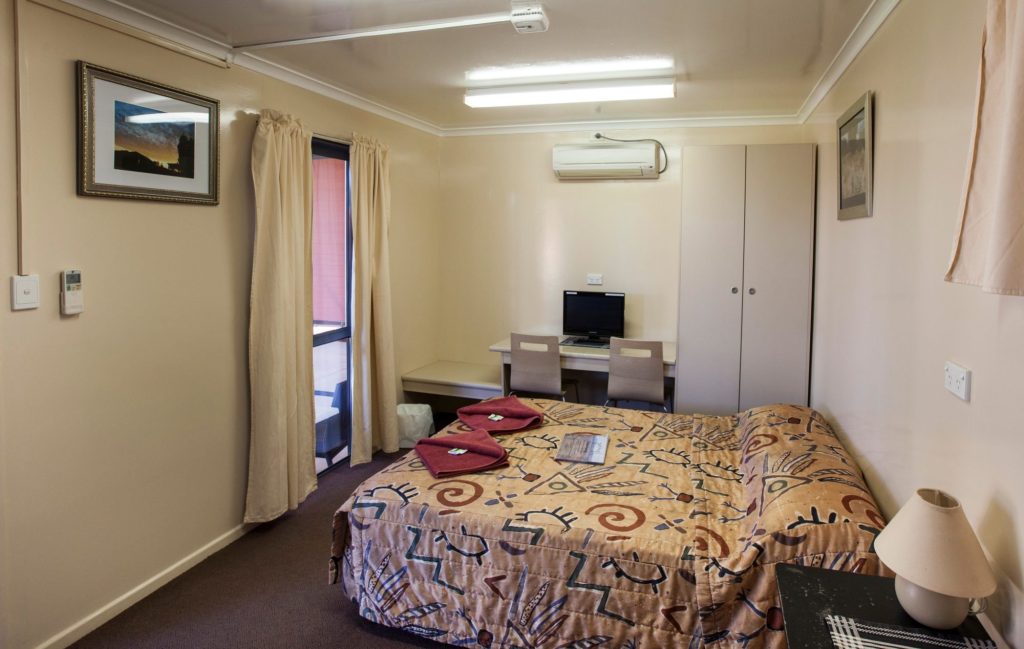 Ensuite room with a double bed, red towels, desk, television and air conditioner