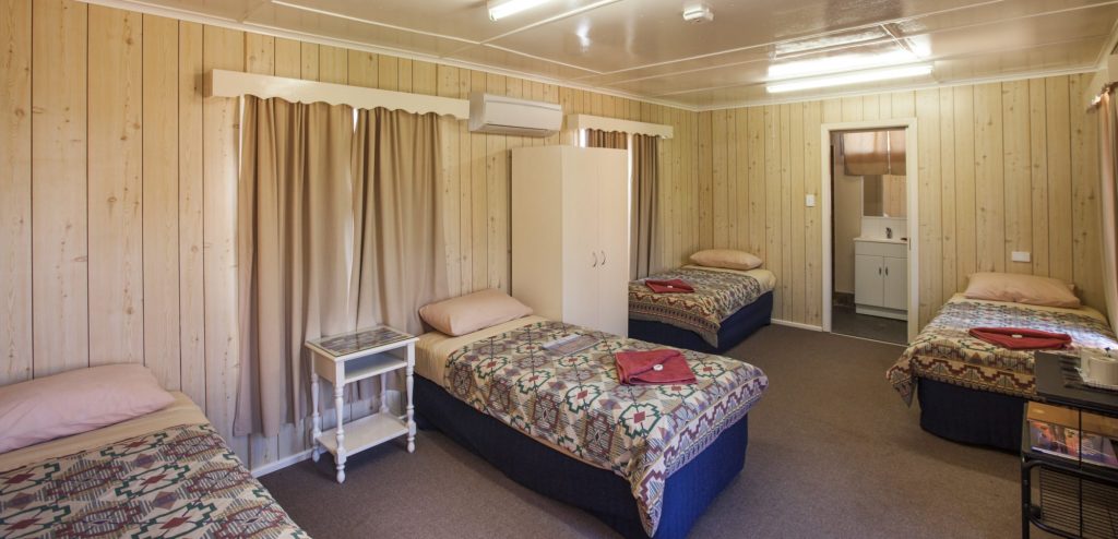 Quad ensuite room with single beds, bedside tables and a doorway to the bathroom