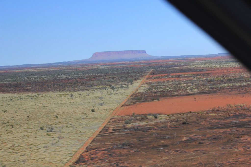 Aerial view of a fire break dividing burnt and unburnt country, with a mesa on the horizon